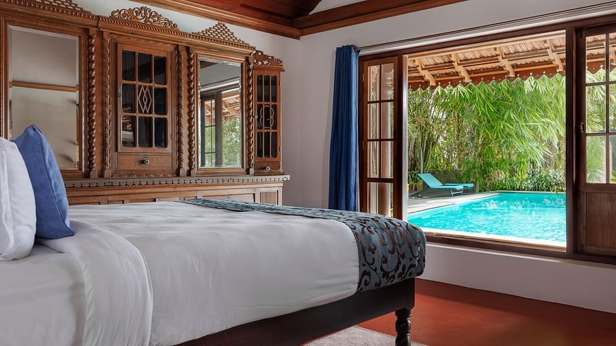A shot of a room taken from an angle showcasing the bed facing a huge window with the view of the pool outside - BluSalzz Villas - Muhamma Resort, Alleppey