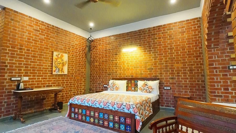 Spacious bedroom with brick walls, patchwork bedding,AC, fan, table and armchair at Tisya Farms, Gurgaon.