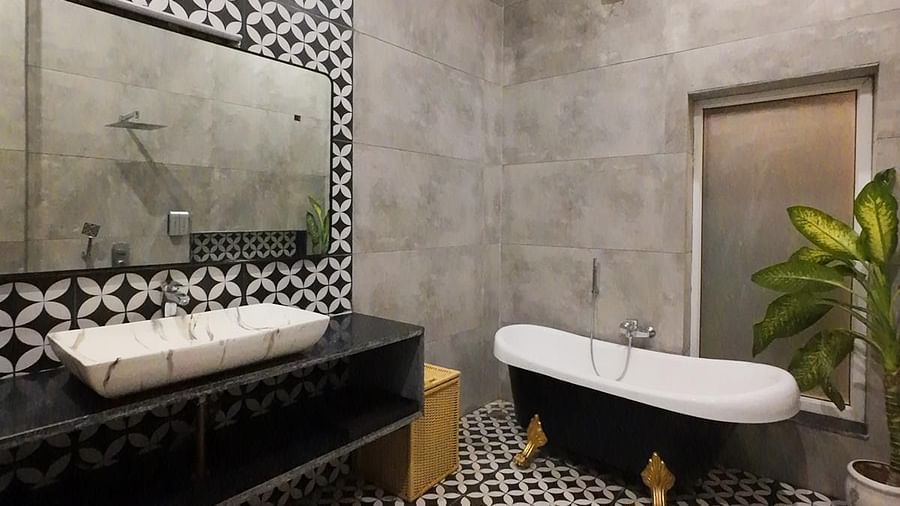 A bathroom at Tisya Farms, Gurgaon with a bathtub, two sinks, patterned flooring, and a concrete wall with a plant in the corner.