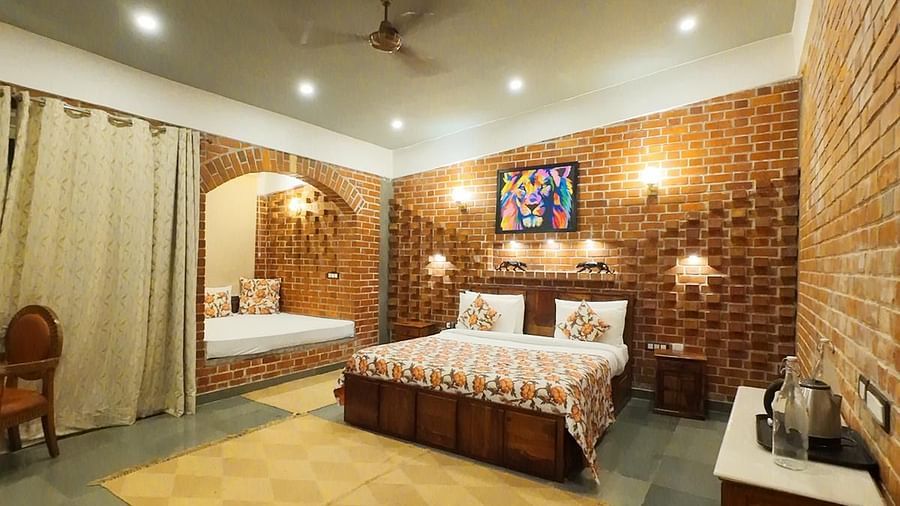 A bedroom at Tisya Farms, Gurgaon with a double bed, yellow-patterned floor mat, brick wall, and ceiling fan.