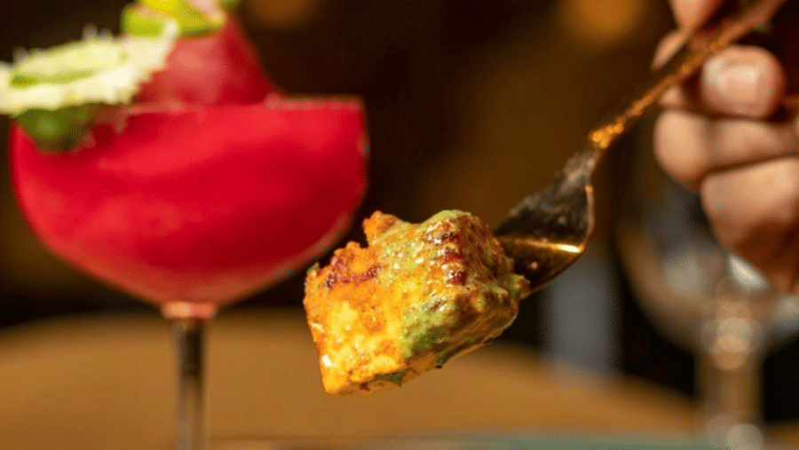 A hand using a fork to lift a piece of food over a plate of grilled paneer cubes at Amantra Shilpi Resort, Udaipur.spicy paneer tikka magic