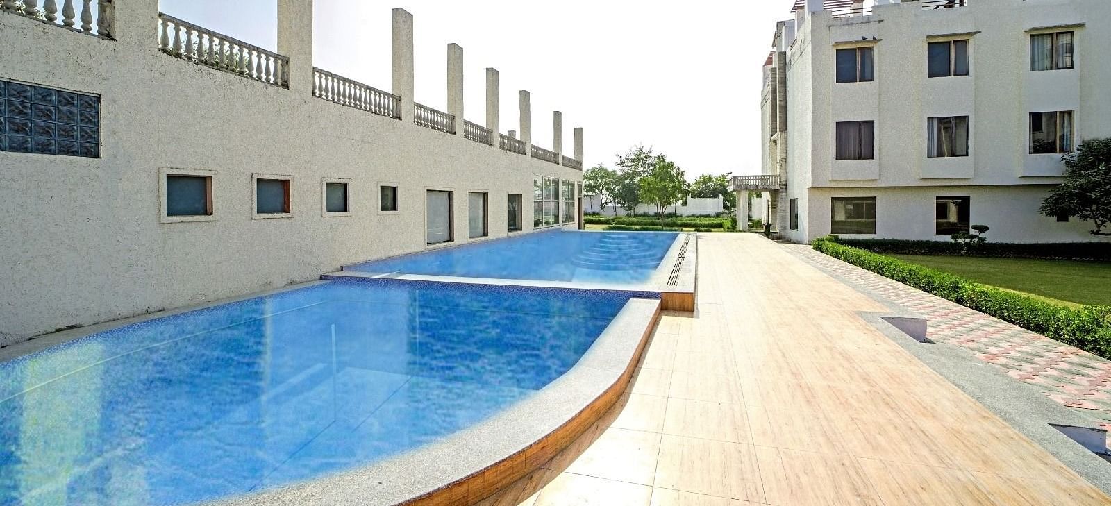 Outdoor swimming pool at Grassfield Riveria Resort, Jaipur, featuring clear water and a wooden deck under bright sunlight.