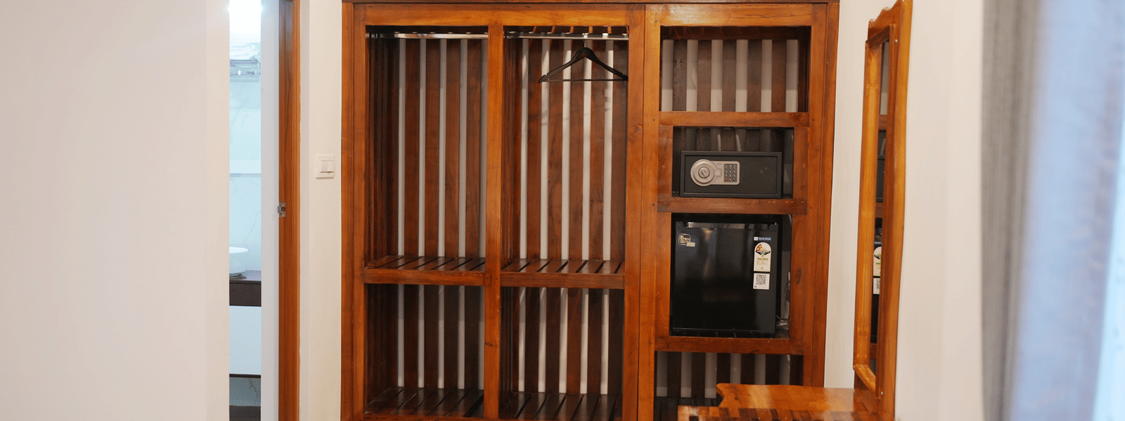 An interior entrance area with a wooden storage cabinet and bench seat next to a doorway at Coorg Orange Blossom Resort and Spa.
