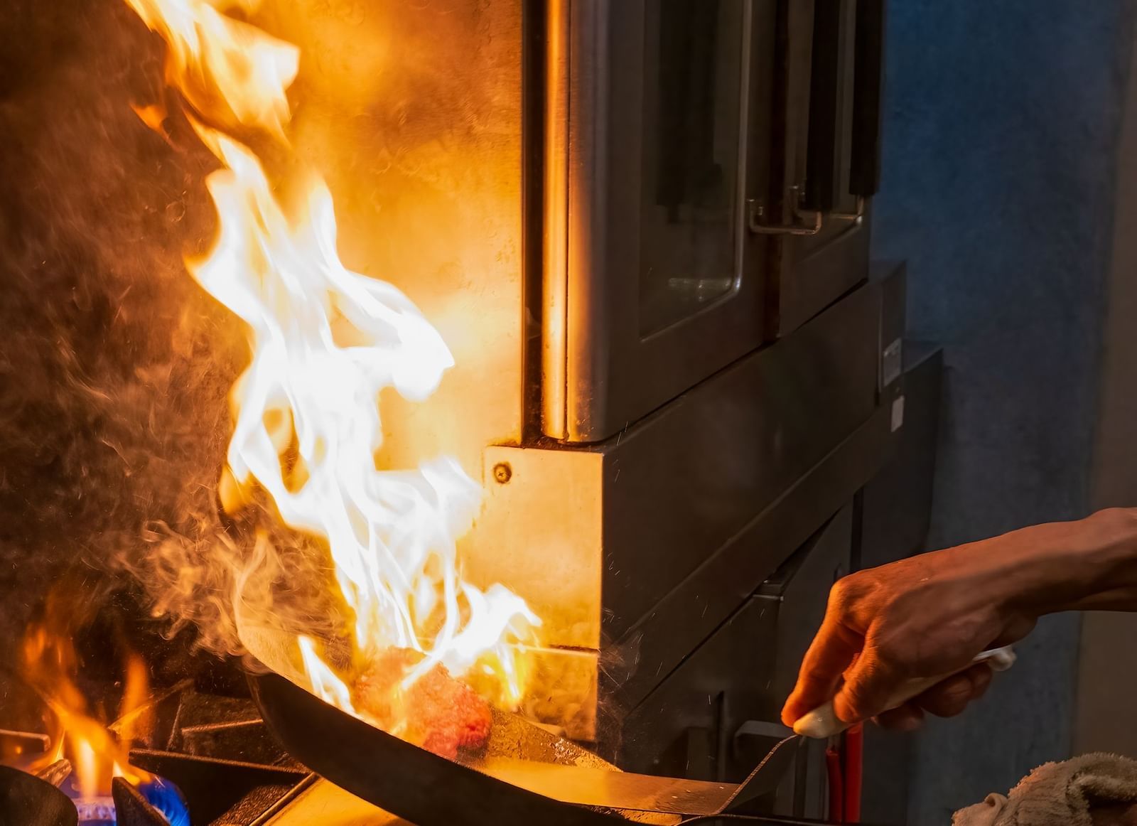 Chef flambéing a dish with open flames in a busy kitchen at The Groveland Hotel.