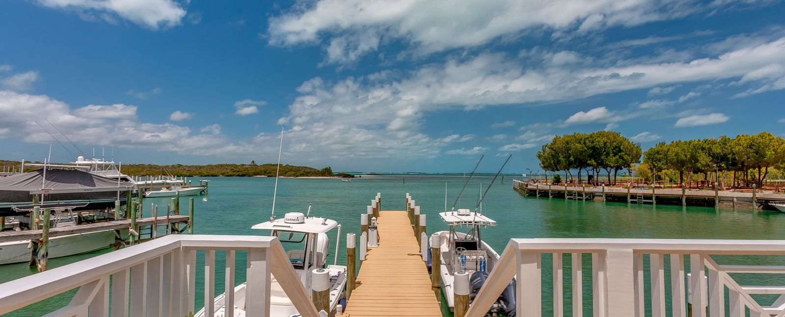 Boardwalk extending over water with white railings, leading to a dock with boats | Abaco Inn