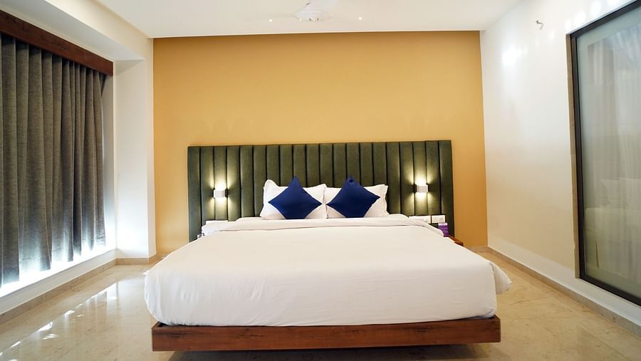 A queen-size bed in well-lit Queen Suite with navy blue cushions and blinds