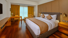 Premium King Room at Pride Hotel Udaipur featuring a plush bed placed in front of the TV mounted on the wall and a work desk placed against the large window partially covered by the curtains