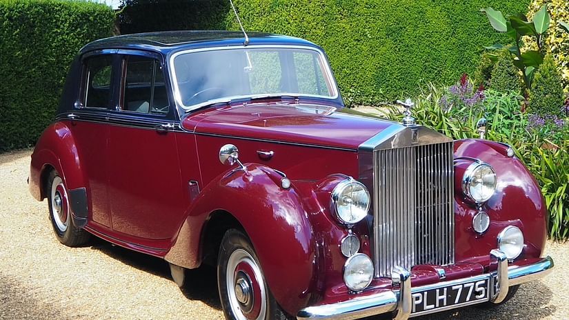 A classic Rolls Royce with sleek silver detailing, elegant curves, and a vintage charm parked in a scenic outdoor setting.