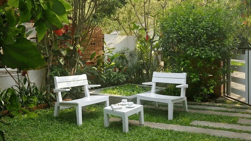 White garden seating set on a green lawn surrounded by trees and plants at Amanvana Spa Resort in Coorg.