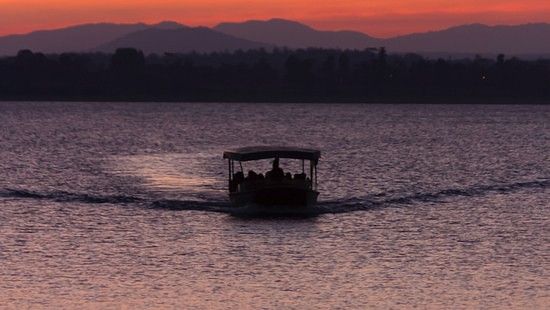 a boat travelling on a waterbody with the sky having different hues after a sunset