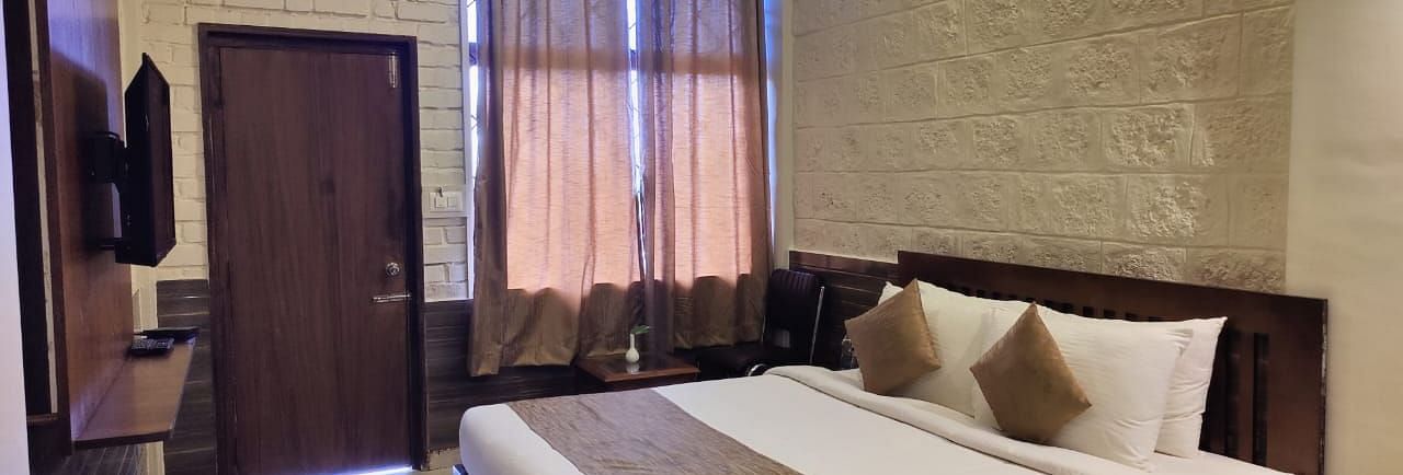Bedroom with a huge bed, bedside table, windows with curtains, wooden door, and a TV | Standard Room | Woodstock Resorts, Coorg