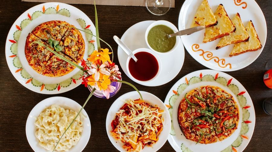 An overhead close-up of a dark table set with 3 plates of curry, small plates of sides, and toast, at Daksh Resort & Amusement Park, Sasan Gir.