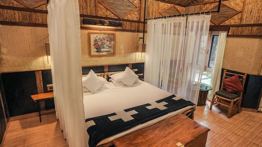 A bedroom with a bed, a chest, and warm lighting, wooden interior - The Den Corbett Resort & Spa, Kumeria.