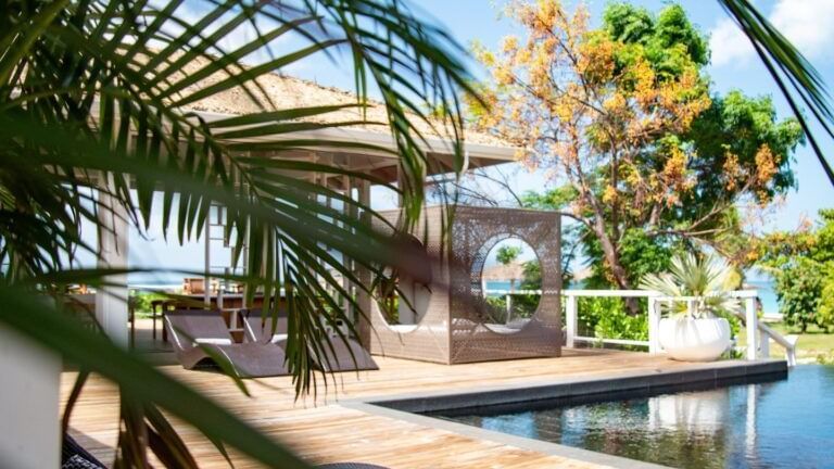 A hammock is set up on a wooden deck surrounded by palm trees and lush greenery.