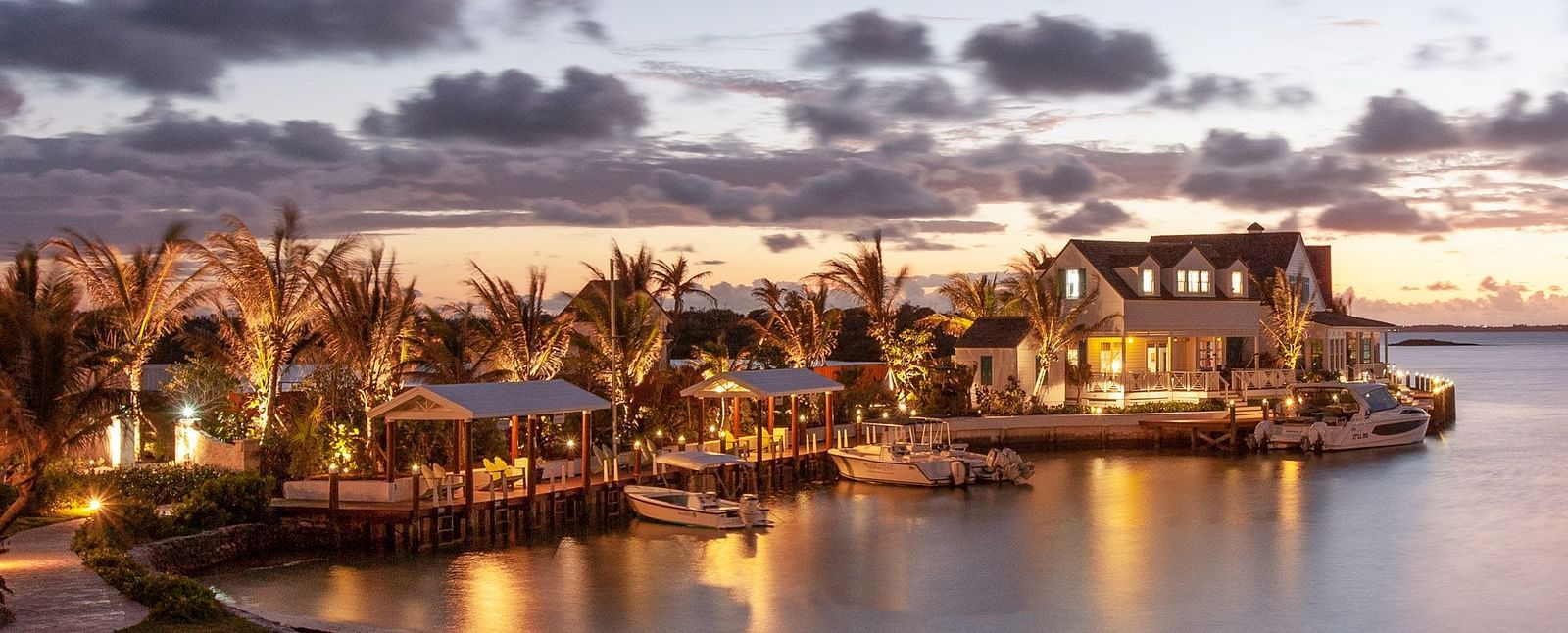 Waterfront buildings glow under dramatic evening skies, with lights reflecting off the calm water in a twilight setting | Abaco Inn
