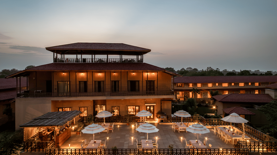 Aerial view of the multi-level structure of AamaGhati Wildlife Resort at nighttime featuring a lit terrace dining space and warm interior lighting.