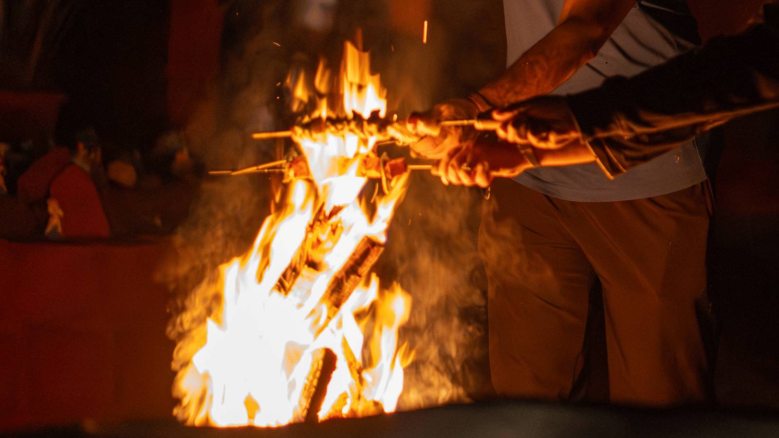 People warming hands over open fire pit with flames rising during nighttime at Tranquil Group.