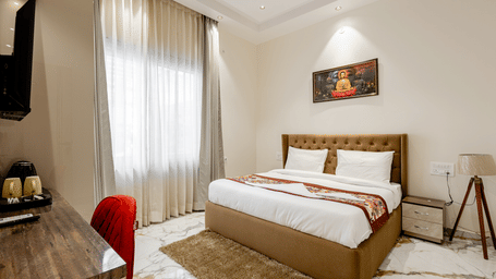 Bedroom of Lime Tree Hotels & Service Apartment Private Limited featuring a wooden bed, a red accent chair, and framed wall art.
