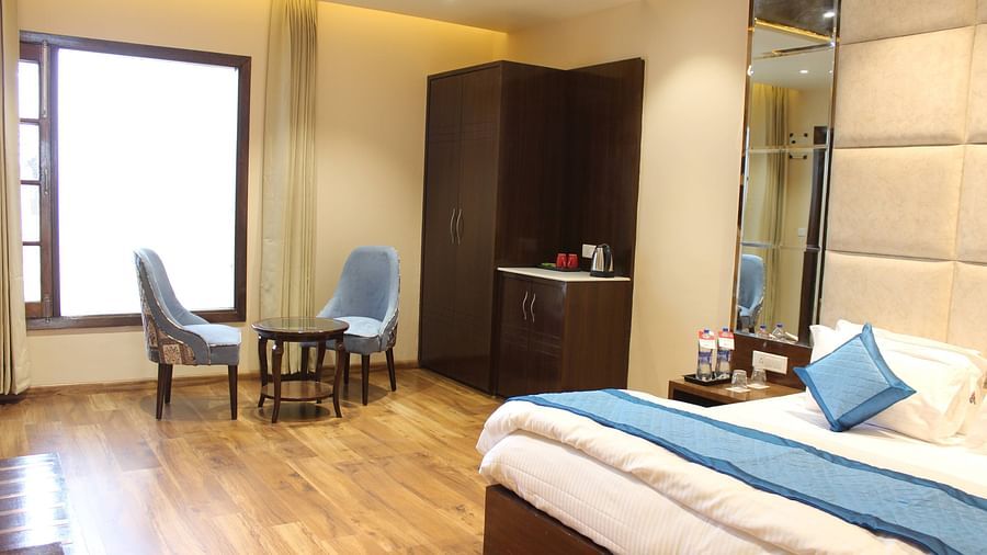 Side angle view of the Superior room with plush bed with bedside tables scenic view from the window with curtains and seating area - Mastiff  Hotel, Dalhousie