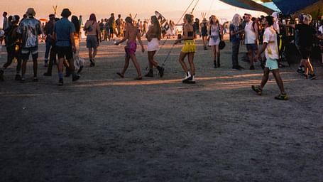 many people walking on the desert with a building in the background