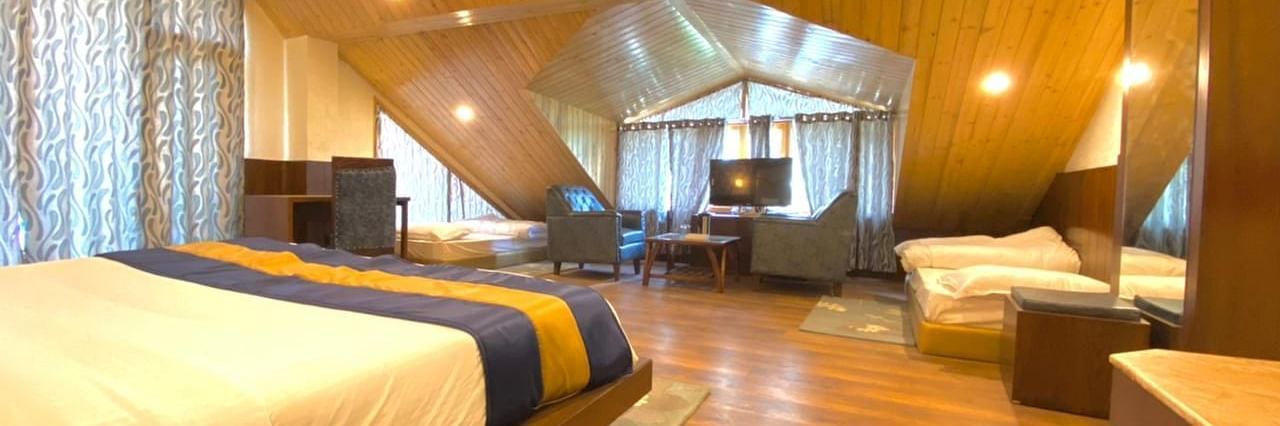 A spacious, well-lit room at La Serene Valley, Manali, with wood-paneled interiors, a large bed, a sitting area, and two single beds.