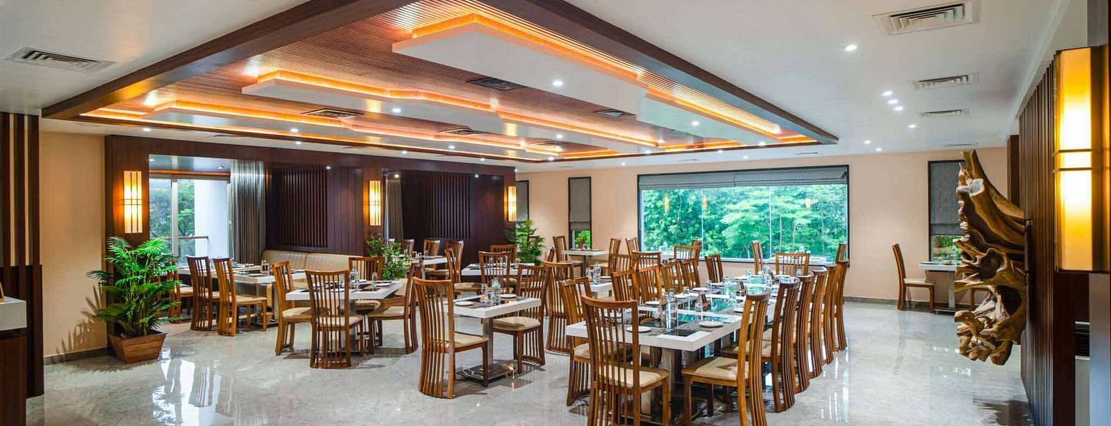 The spacious and well-lit dining hall at Mansha Palace features numerous set tables and comfortable wooden chairs.
