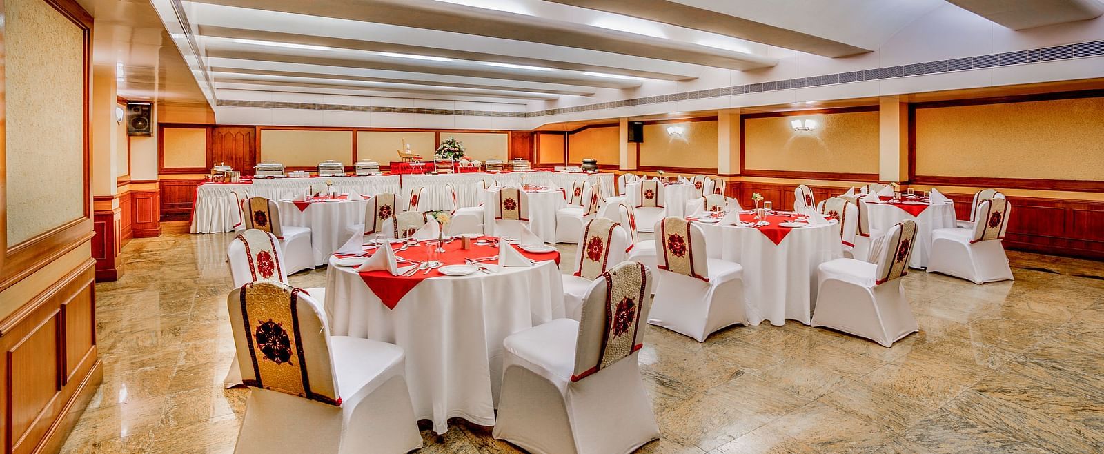 A spacious banquet hall with set tables and red chairs at Tara, Comfort Hotel in Hyderabad - Ramoji Film City.