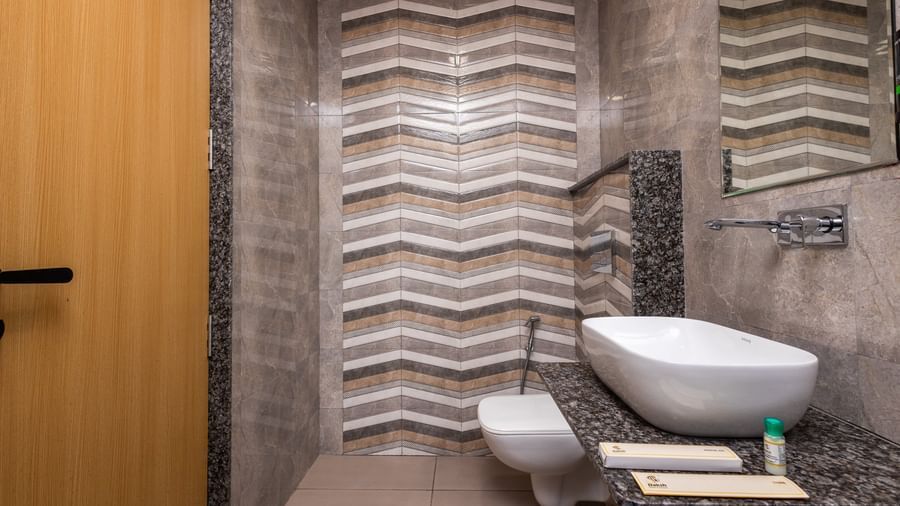  A bathroom at Daksh The Grand Gowardhan, Dwarka, showcasing chevron tiles, a toilet, and a sleek wash basin with new utilities.