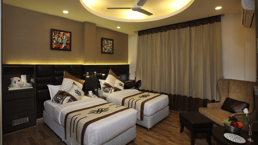 A Superior Twin Bed Room at JRD Exotica - Business Hotel featuring twin beds, an armchair with an ottoman, and modern lighting.