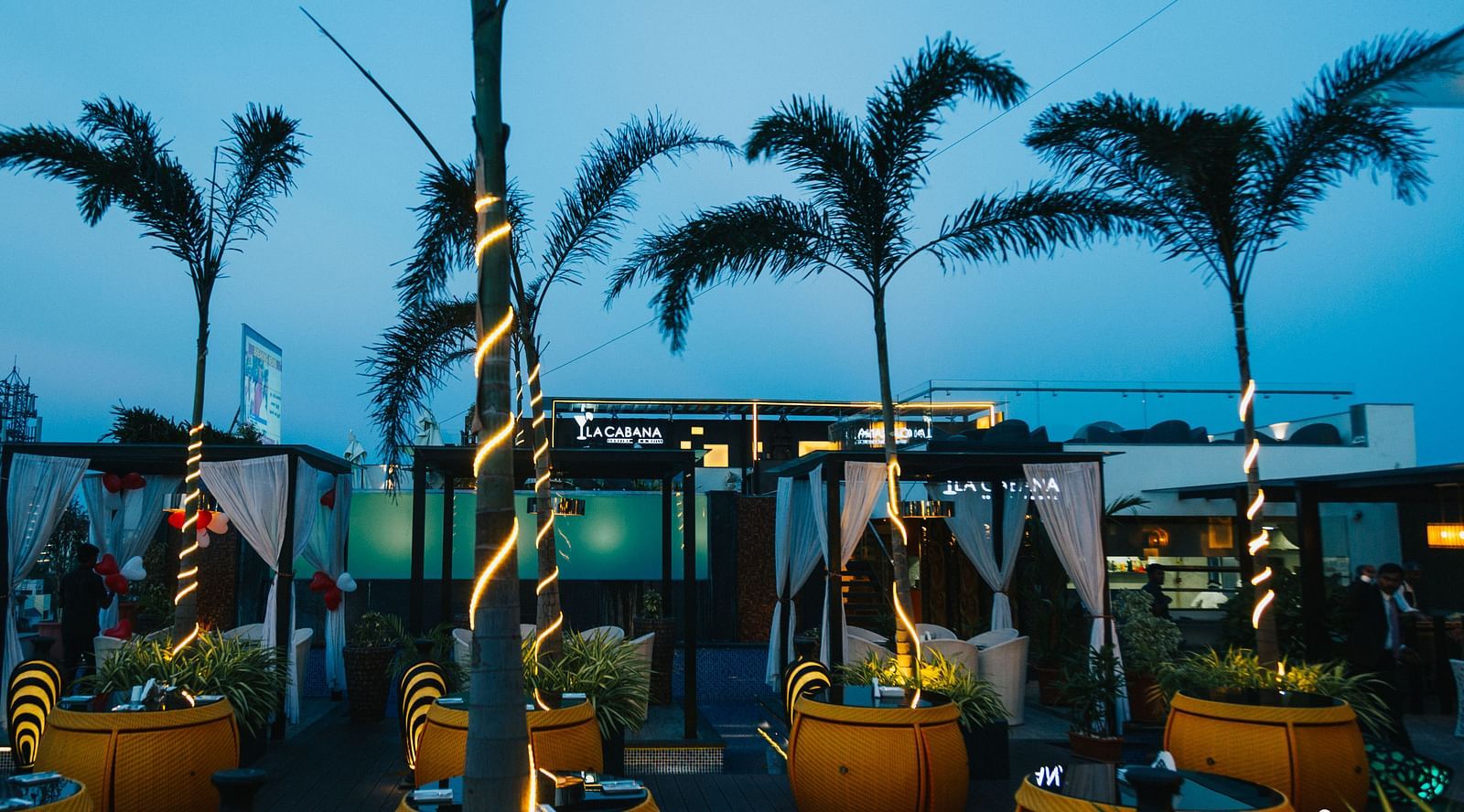 chairs with tables placed across a space with decorated trees in between them - Hotel Park Elanza, Chennai
