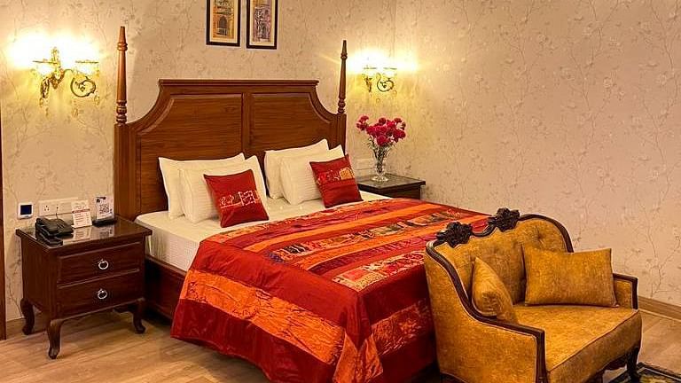 Elegant bedroom at Hotel Mount View featuring a wooden four-poster bed with vibrant red linens, ornate chandelier, floral wallpaper, side tables, cosy upholstered seating.