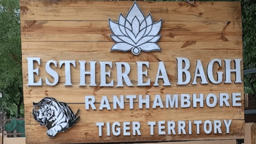 A wooden entrance sign for Estherea Bagh, Ranthambore - Tiger Territory, featuring a lotus logo and a tiger illustration.