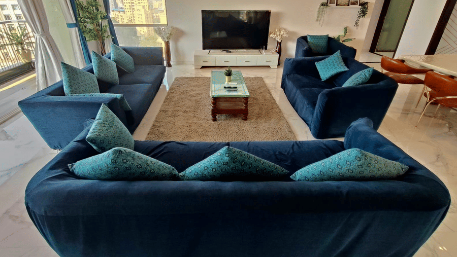 2hall and living room area of Maxxvalue Hotel, Chitranjan Tower, Powai with blue themed couch and a dining table in the corner of the room