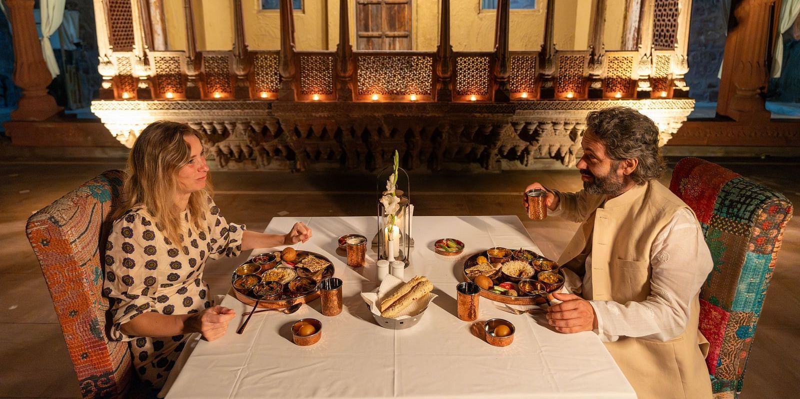 A man and woman in a dining area with an assortment of food placed on the table at Aerial view of a swimming pool with lounge chairs on the side at Surpura Bagh.
