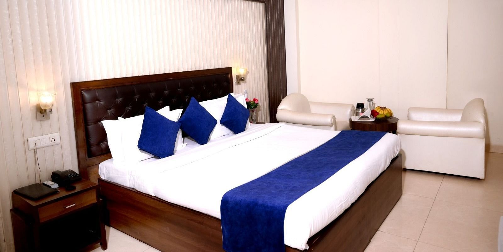 A spacious hotel room with a king-size bed, blue and white bedding, plush headboard, and elegant lighting - Hotel Diamond Inn, Chandigarh