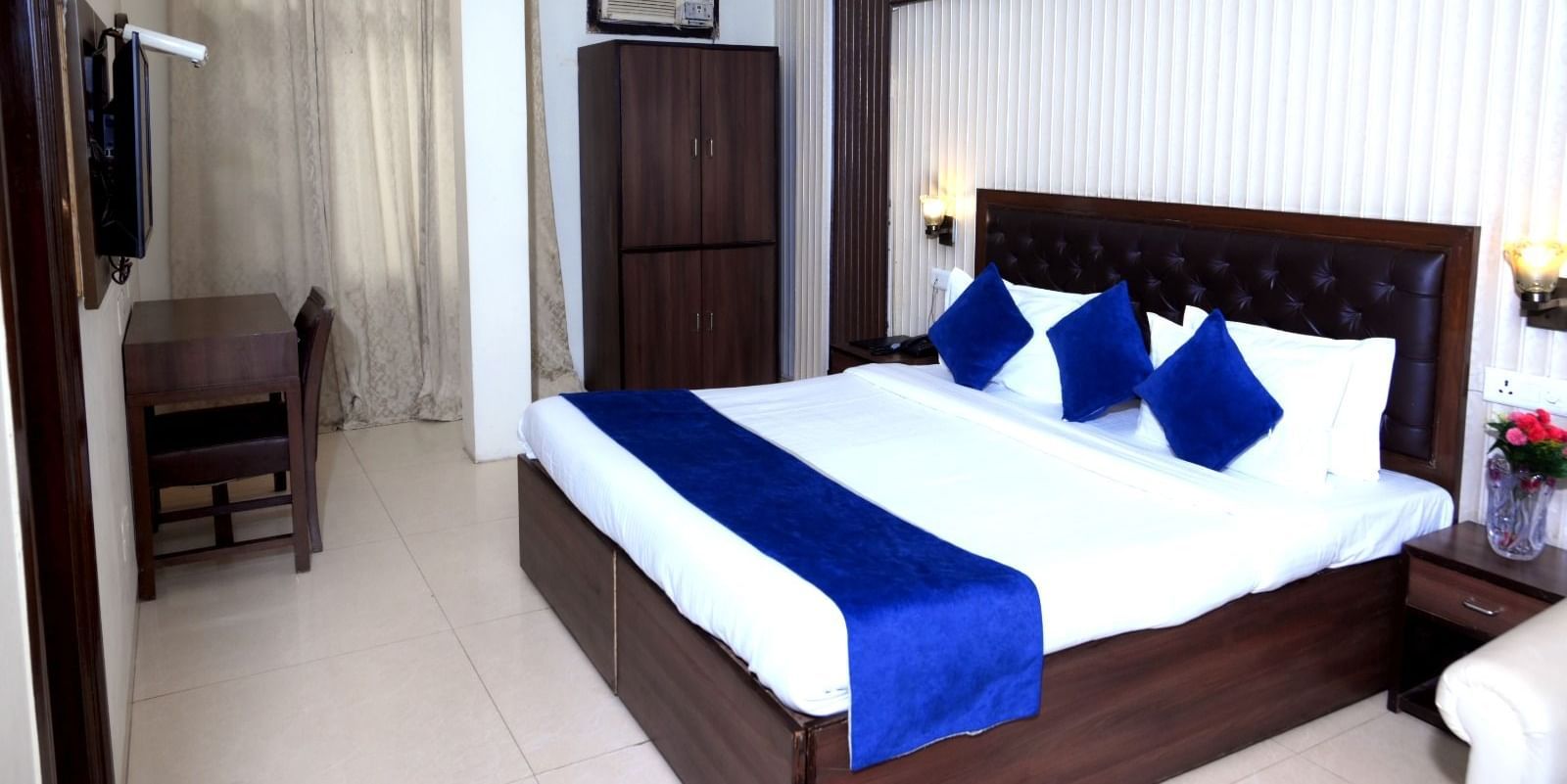 Neat hotel room at Hotel Diamond Inn, Chandigarh featuring king-size bed with blue wraps, a work desk, wooden wardrobe and bedside table.