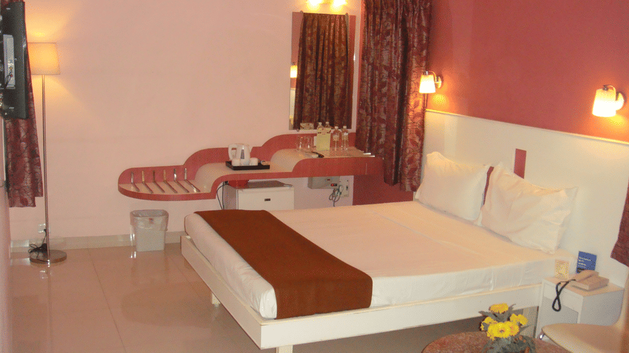 A well-appointed hotel bedroom with a double bed, soft pink and dark maroon walls, and a dedicated vanity mirror desk - Hotel Pandian