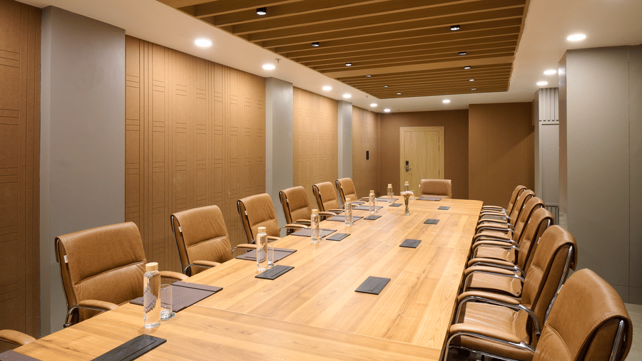A conference or boardroom setup with a long wooden table, multiple executive chairs, and wood panelling on the walls and ceiling | Voyage Eastin Suites