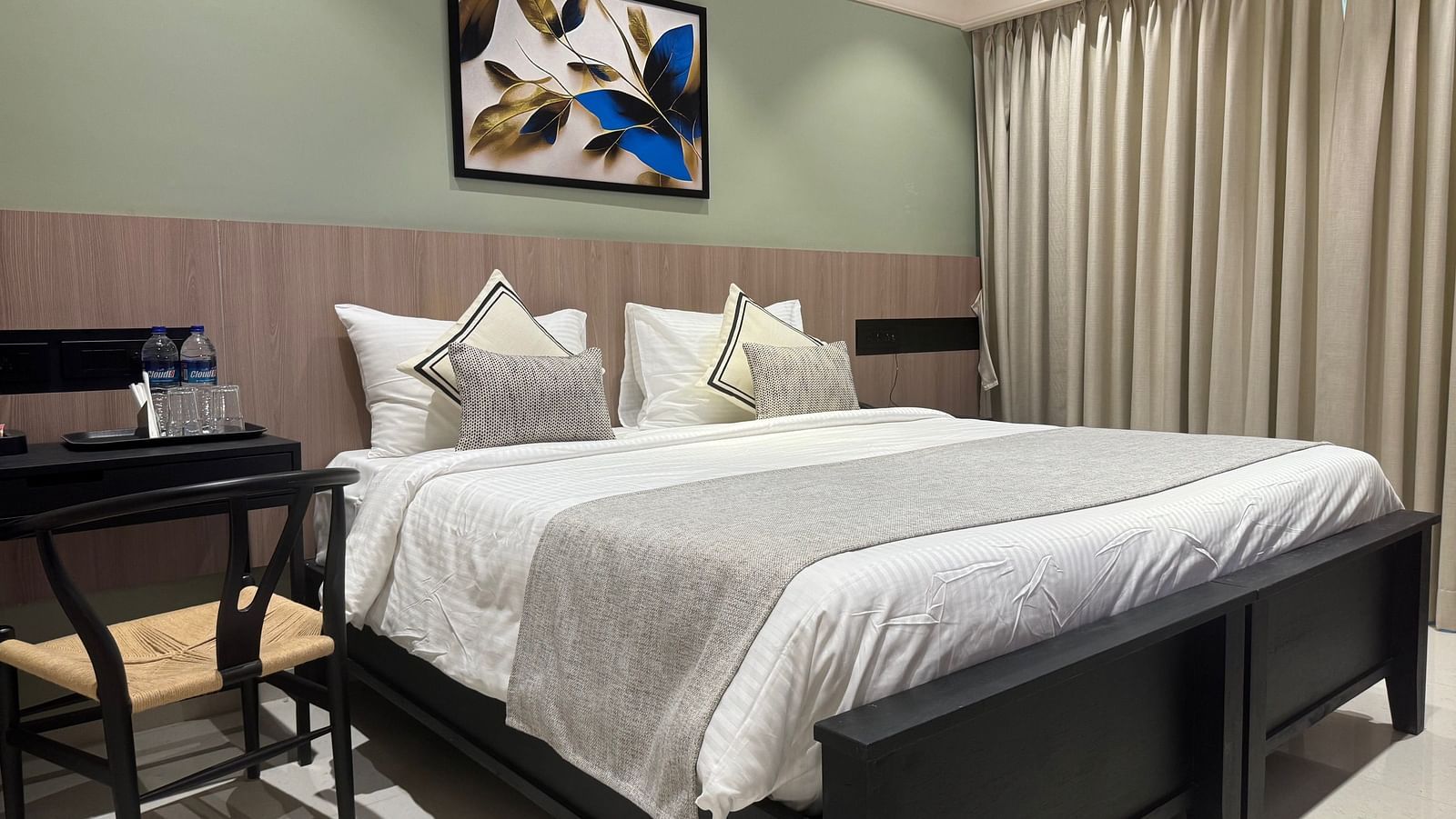 A king bed with a painting hung above it and study table beside it inside deluxe room - Hotel Mumbai House, Valnai, Malad