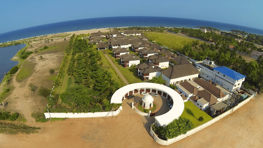 An aerial view of a coastal resort featuring multiple buildings, green spaces, and a semi-circular driveway next to the sea | Le Pondy