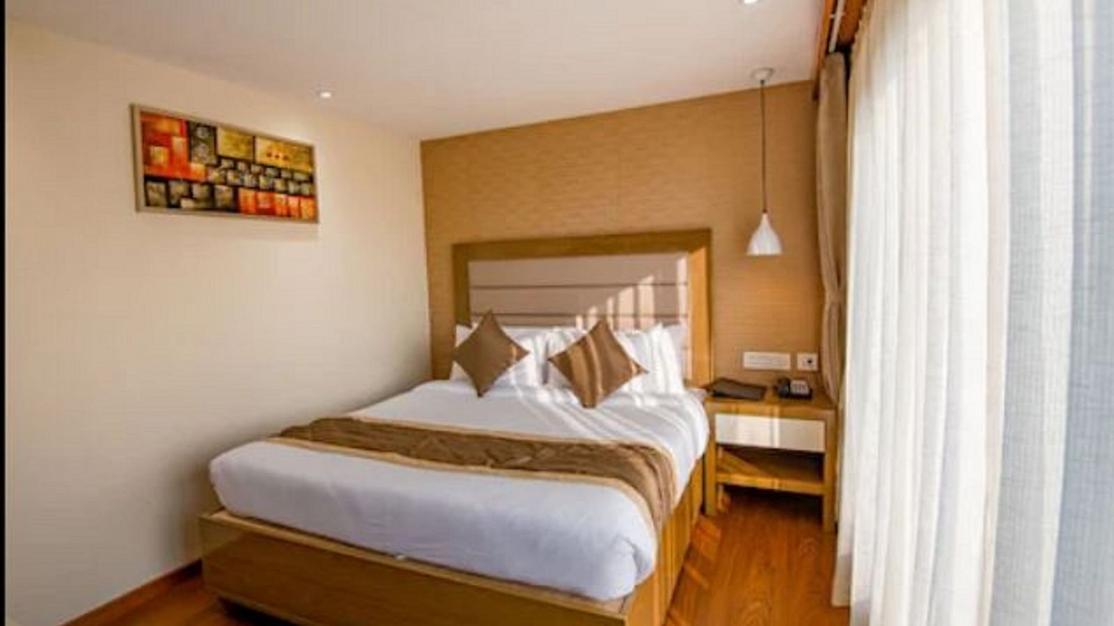A bright and neatly arranged standard hotel room with a comfortable bed, a small desk, and an abstract painting above the bed at Yashshree The Imperial Inn, Siliguri.