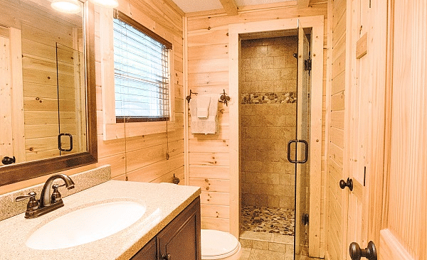 a shower cubical at the far end of the bathroom separated by a glass door with a wash basin and a commode beside it - Historic Tapoco Lodge