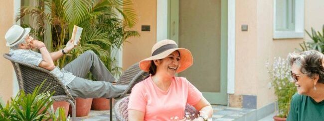 Three people sitting on a patio outside a peach coloured building, engaged in conversation at Karma Chalets.