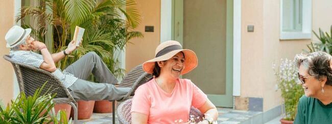 Three people sitting on a patio outside a peach coloured building, engaged in conversation at Karma Chalets.