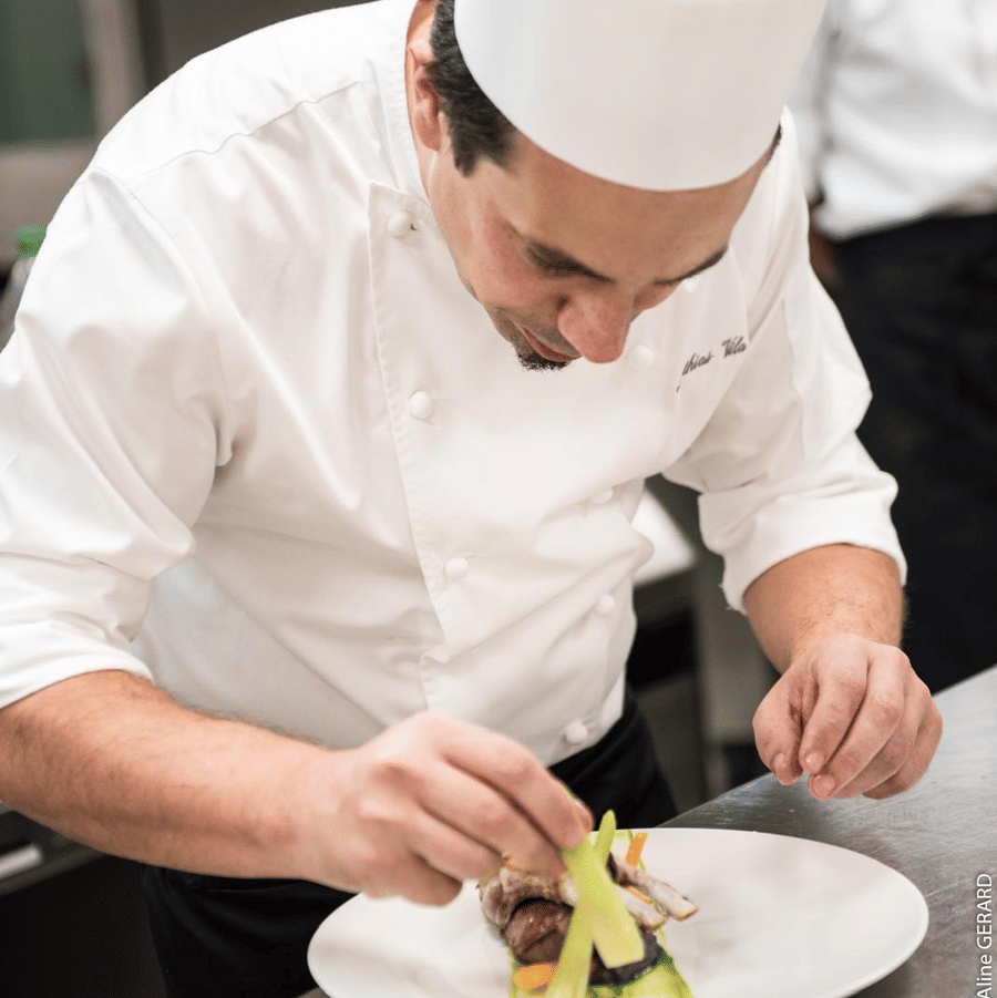 Chef Mathias carefully garnishing a plate in the kitchen, demonstrating the precision and artistry behind the Taste of France culinary experience.