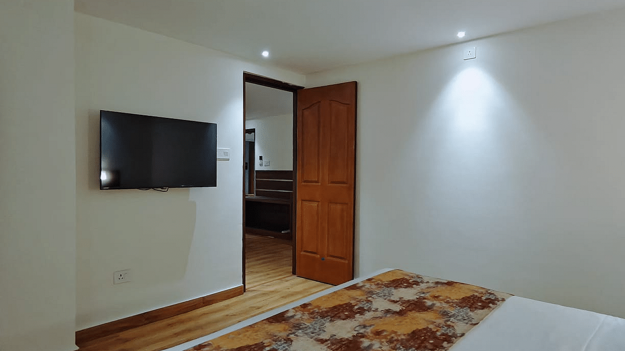 A close-up shot of a bed and a tv mounted on the wall with a open door - Sumitel JB Park, Darjeeling