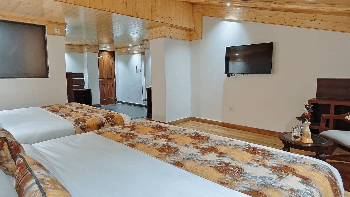 A modern, well-appointed room featuring two beds with crisp white linens and patterned runners, a wall-mounted tv, and an elegant wooden ceiling - Sumitel JB Park, Darjeeling