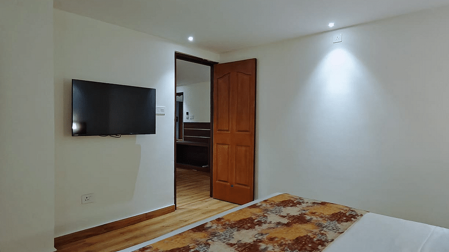 A close-up shot of a bed and a tv mounted on the wall with a open door - Sumitel JB Park, Darjeeling