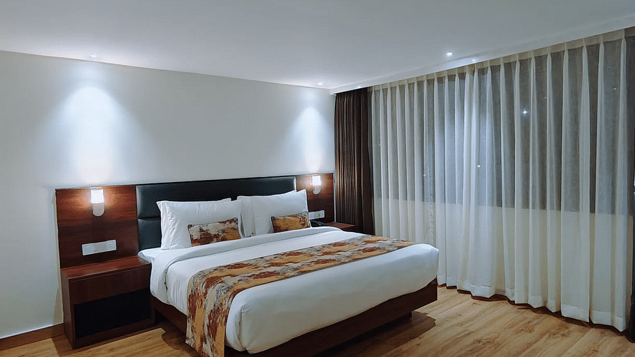 A wide angle of a bed with white linnen and a patterned runner on it under a warm lighting - Sumitel JB Park, Darjeeling