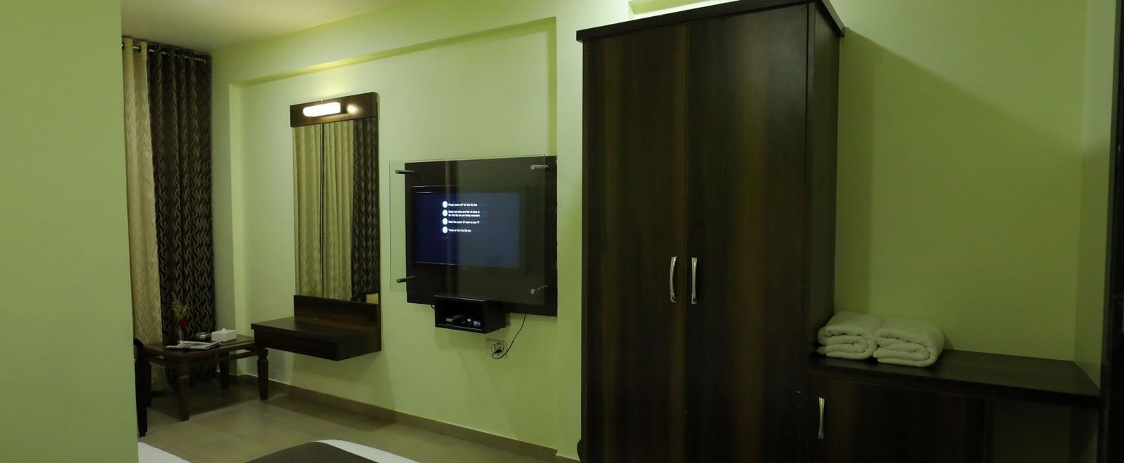 A clean and well-lit bedroom at Krushnai Resort featuring a dark wooden wardrobe and a TV.